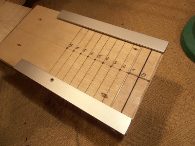 Tutaj jeden z moich patentów na ustawianie kąta gryfu w czasie montażu instrumentu. Ruchoma , przezroczysta płyta z poliwęglanu z linia ... natomiast pod spodem podziałka .... . Płytka przesuwa sie po prostych prowadnikach z kątowników alu  i ma grubość 2